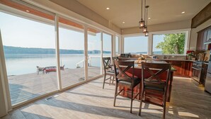 A spacious kitchen with large windows overlooking a lake, a dining area with wooden chairs, and a view of the water.