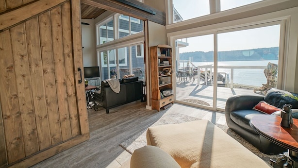 A spacious living room with a large sliding glass door leading to a deck overlooking a body of water.