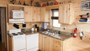 Une cuisine compacte avec des meubles en bois, un four à micro-ondes, une cuisinière et un lave-vaisselle. Des objets décoratifs sont disposés sur les étagères et un extincteur est fixé au mur.