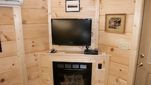 Une pièce chaleureuse avec une cheminée, un téléviseur fixé au mur et des murs en bois.