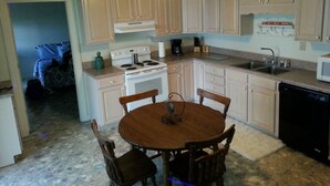 A compact kitchen with white cabinets, a stove, a sink, and a dishwasher. There is a wooden dining table with four chairs. - Relatively Secluded Location Yet Only 10 Minute Drive To Pubs And Restaurants. (Chocowinity)