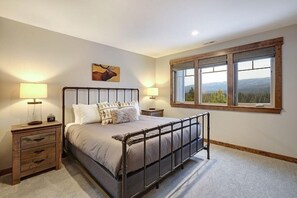 Quarto com estrutura de cama de metal, uma janela ampla com vista para o exterior e duas mesas de cabeceira com luminárias.