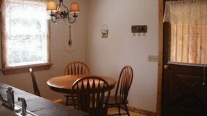 A dining area with a round table, four wooden chairs, a chandelier, and a window with blinds.