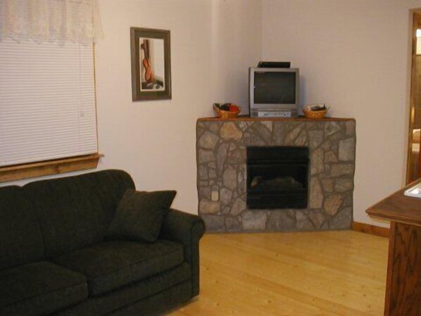 A living room with a stone fireplace, a television on top, and a green sofa. - Family friendly cabins near Galax, VA & the Blue Ridge Music Center (Galax)
