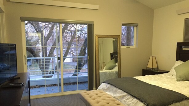 Ein Schlafzimmer mit einem großen Bett, einer Bank, einem Fernseher und einer Glastür, die auf einen Balkon führt.