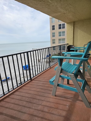 Ein Balkon mit Blick auf Strand und Meer, ausgestattet mit einem Geländer und zwei blauen Stühlen.