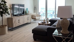 En moderne stue med et stort fladskærms-tv, en sofa, et sofabord og en potteplante.