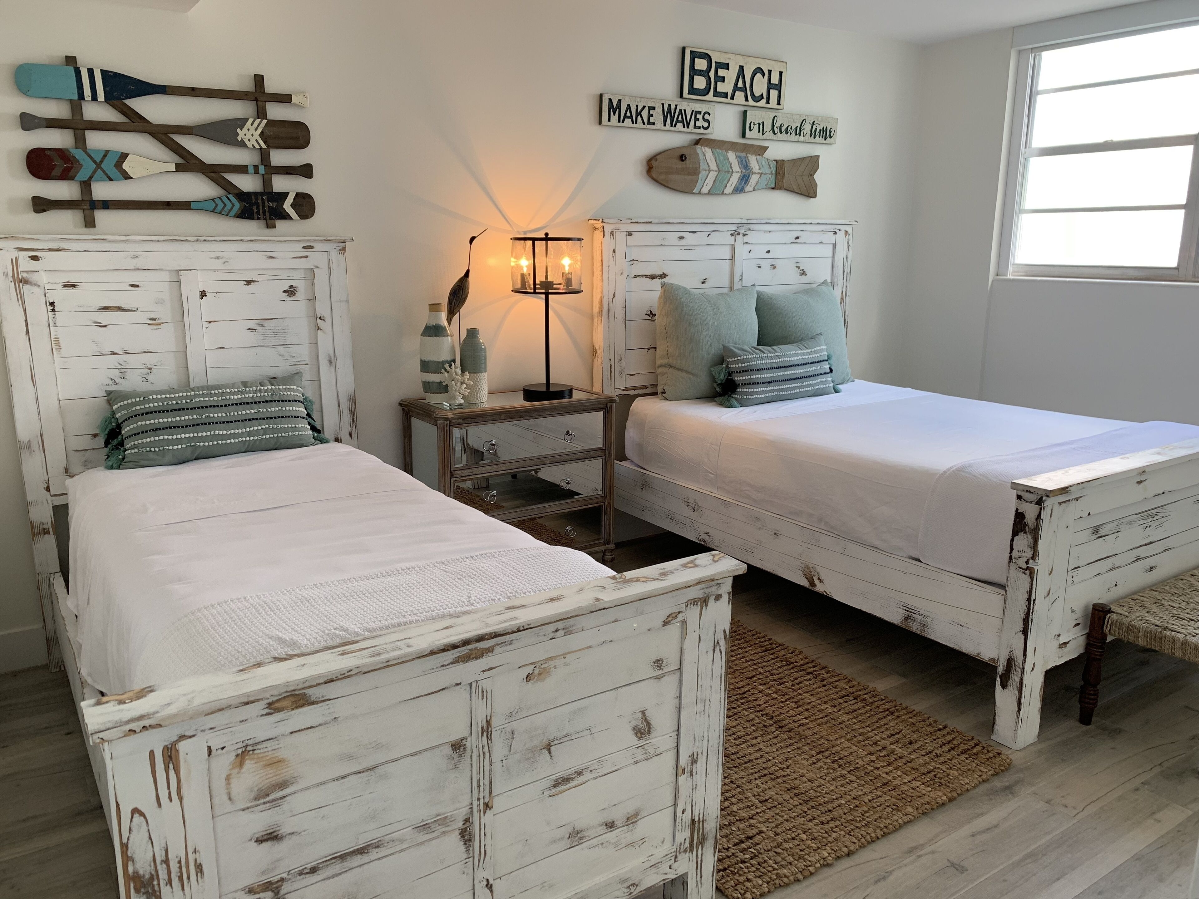 Une chambre à coucher avec deux lits blancs, une table de chevet, une lampe et des décorations murales, notamment un poisson et une planche de paddle.