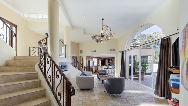 A spacious living area with a staircase, a chandelier, and a large window offering a view of the outdoors.