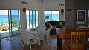 A spacious living area with a large sliding glass door leading to a balcony overlooking the ocean. - Oceanfront Glass House on  Deserted Pink Sand Beach-directly on beach!  (Governors Harbour)