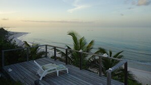A wooden deck with a white lounge chair and a railing overlooking a beach and ocean. - Oceanfront Glass House on  Deserted Pink Sand Beach-directly on beach!  (Governors Harbour)