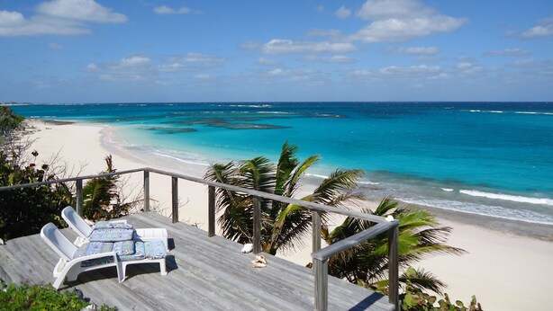 A beach view with a wooden deck, lounge chairs, and palm trees. - Oceanfront Glass House on  Deserted Pink Sand Beach-directly on beach!  (Governors Harbour)