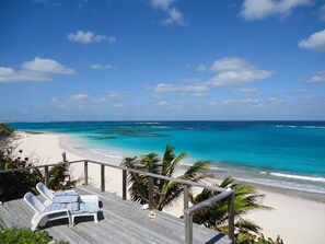 Een uitzicht op het strand met een houten terras, ligstoelen en palmbomen.
