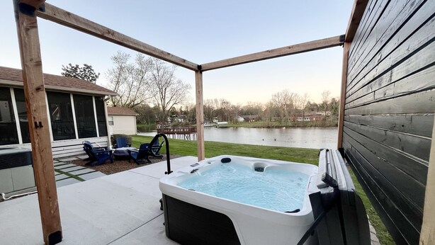 A hot tub in an outdoor wooden deck area with a view of a lake and houses in the background. - NASH Lakehouse 5 bedroom 30 mins to downtown  (Mount Juliet)