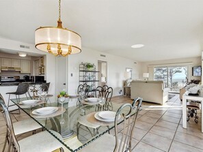 A spacious dining area with a glass table and metal chairs, a kitchen with modern appliances, and a balcony with a view.