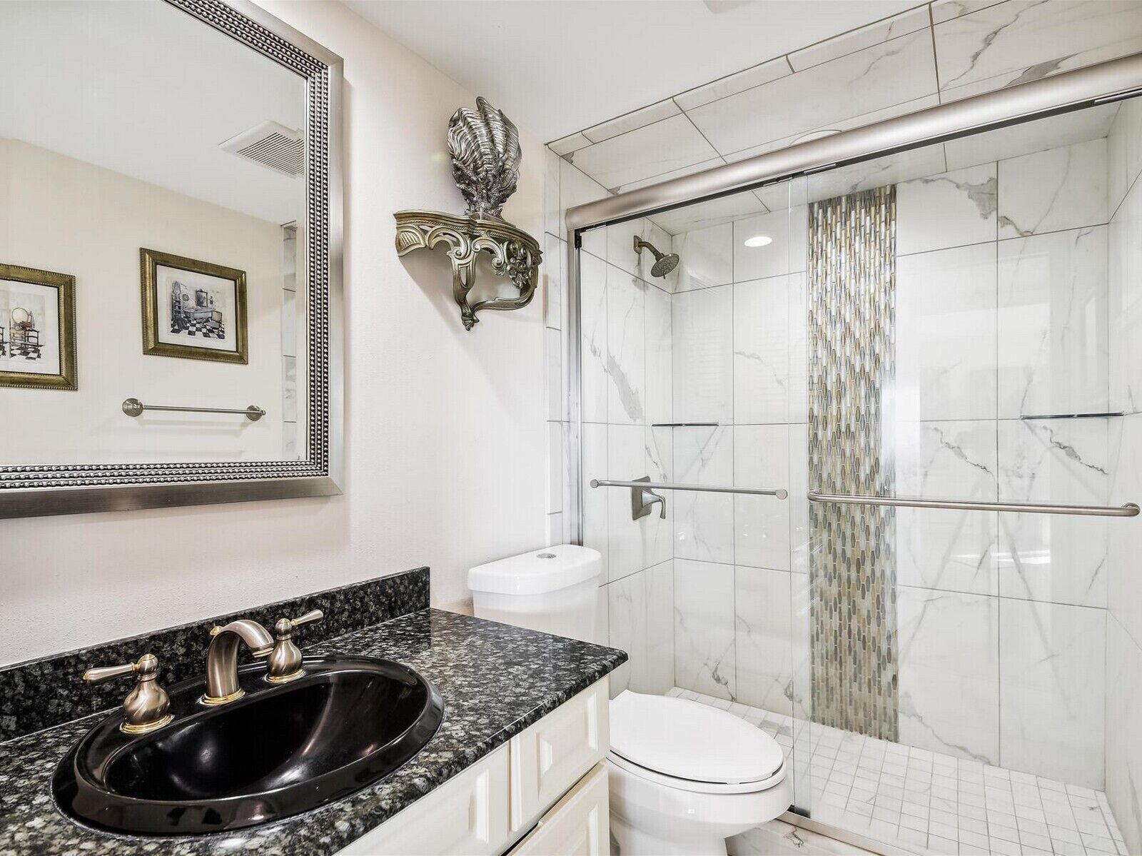 A bathroom with a black sink, white toilet, and a glass-enclosed shower with marble tiles.
