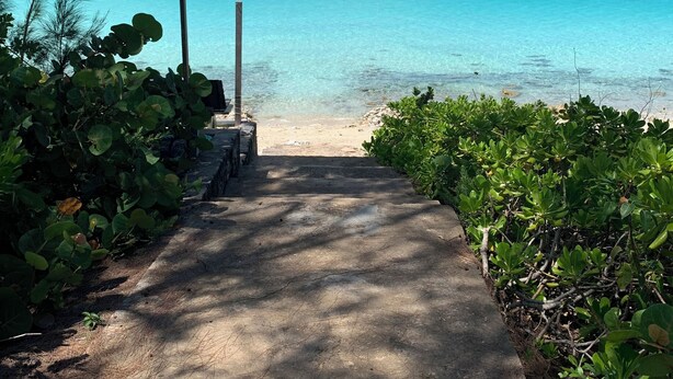 Un sendero de concreto que lleva a una playa con agua turquesa cristalina y un cielo despejado.