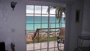Una habitación con puerta corrediza de vidrio que da a vista de playa, una mesita con una piña y una silla.