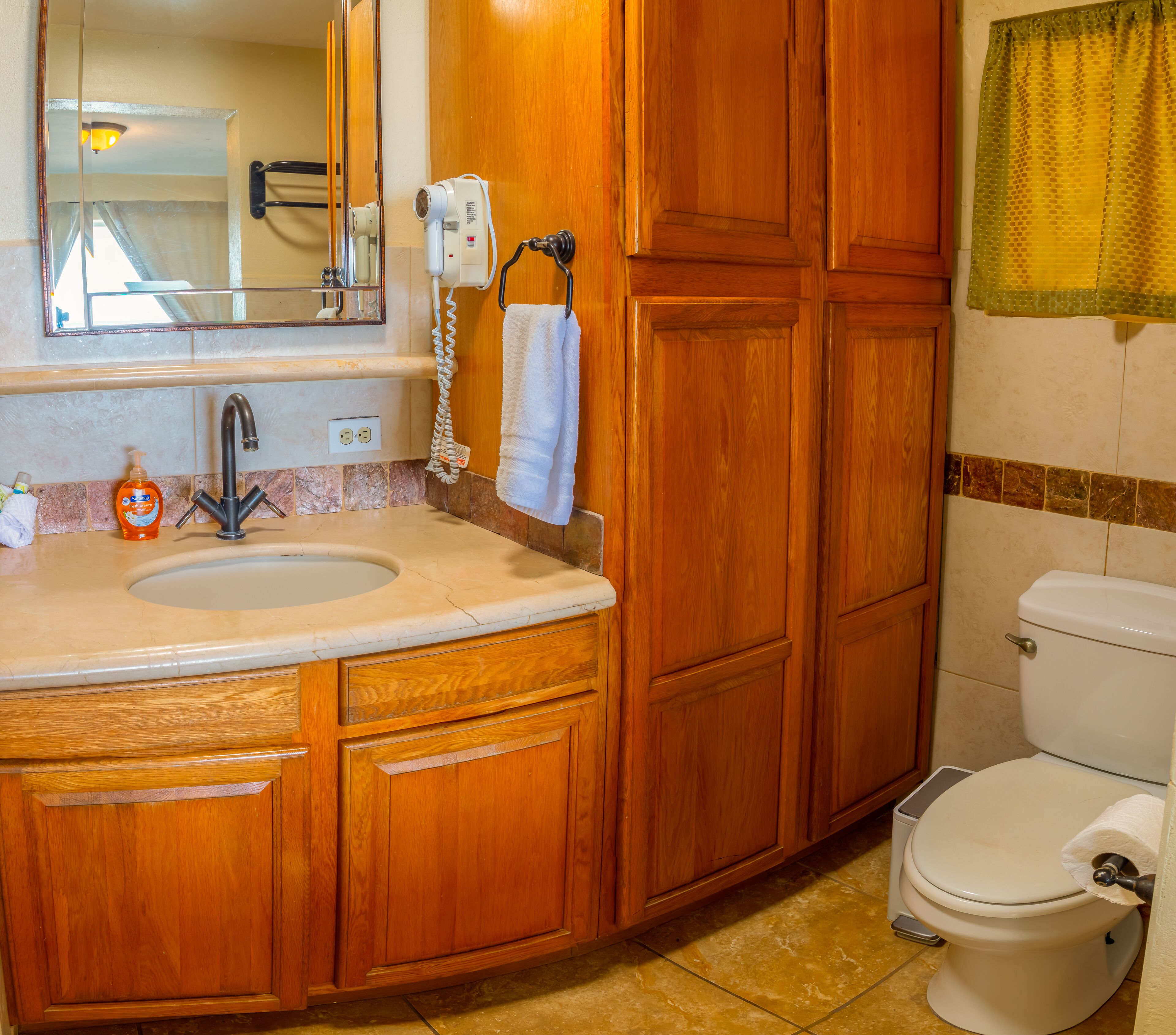 Une salle de bain avec des meubles en bois, un lavabo, un miroir, un sèche-cheveux et des toilettes.
