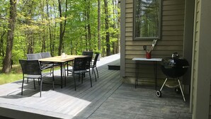 Eine Terrasse mit Tisch, Stühlen, einem Grill und einem Fenster mit Blick auf einen Wald.