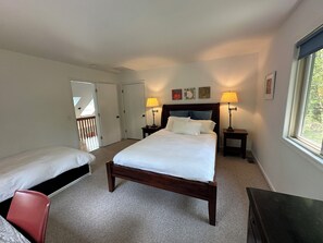 A bedroom with a large bed, two bedside tables with lamps, a red chair, and a view of the outdoors through a window.