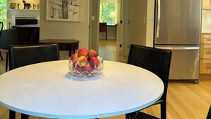 Eine moderne Küche mit einem Edelstahl-Kühlschrank, einem Esstisch mit Stühlen und einer Obstschale auf dem Tisch.