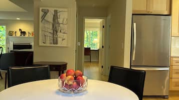A modern kitchen with a stainless steel refrigerator, a dining table with chairs, and a bowl of fruit on the table.