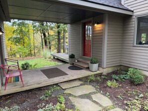 A house with a covered porch, a red door, and a small garden area with stepping stones and potted plants.