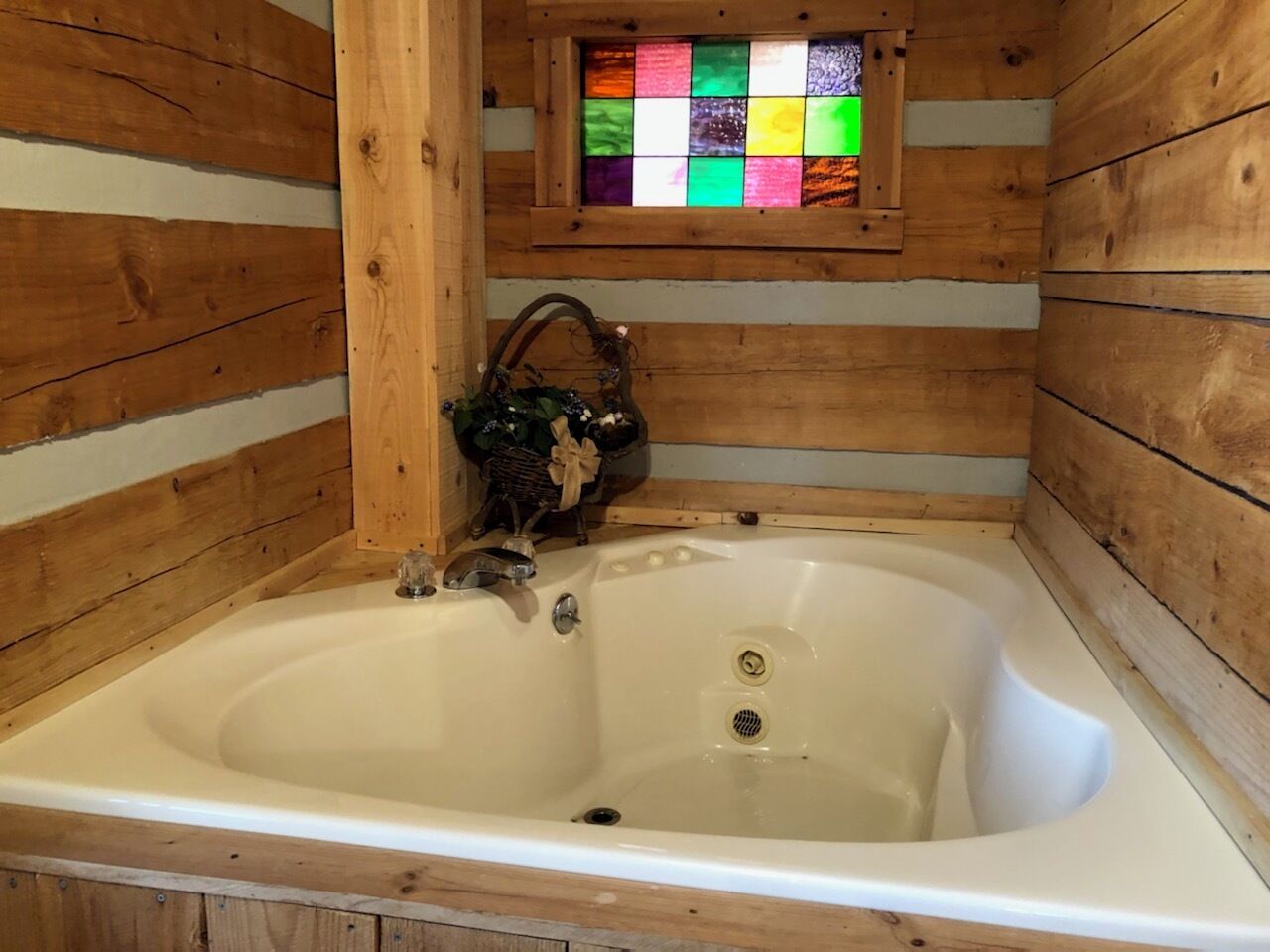 A wooden cabin with a large bathtub, a small stained glass window above the tub, and a rustic interior.