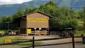 A wooden building labeled "Davy Crockett Riding Stables" with a horse trough and a sign indicating a horse route. - Cabin with beautiful view, on 'Peaceful Side of the Smokies' (Townsend)