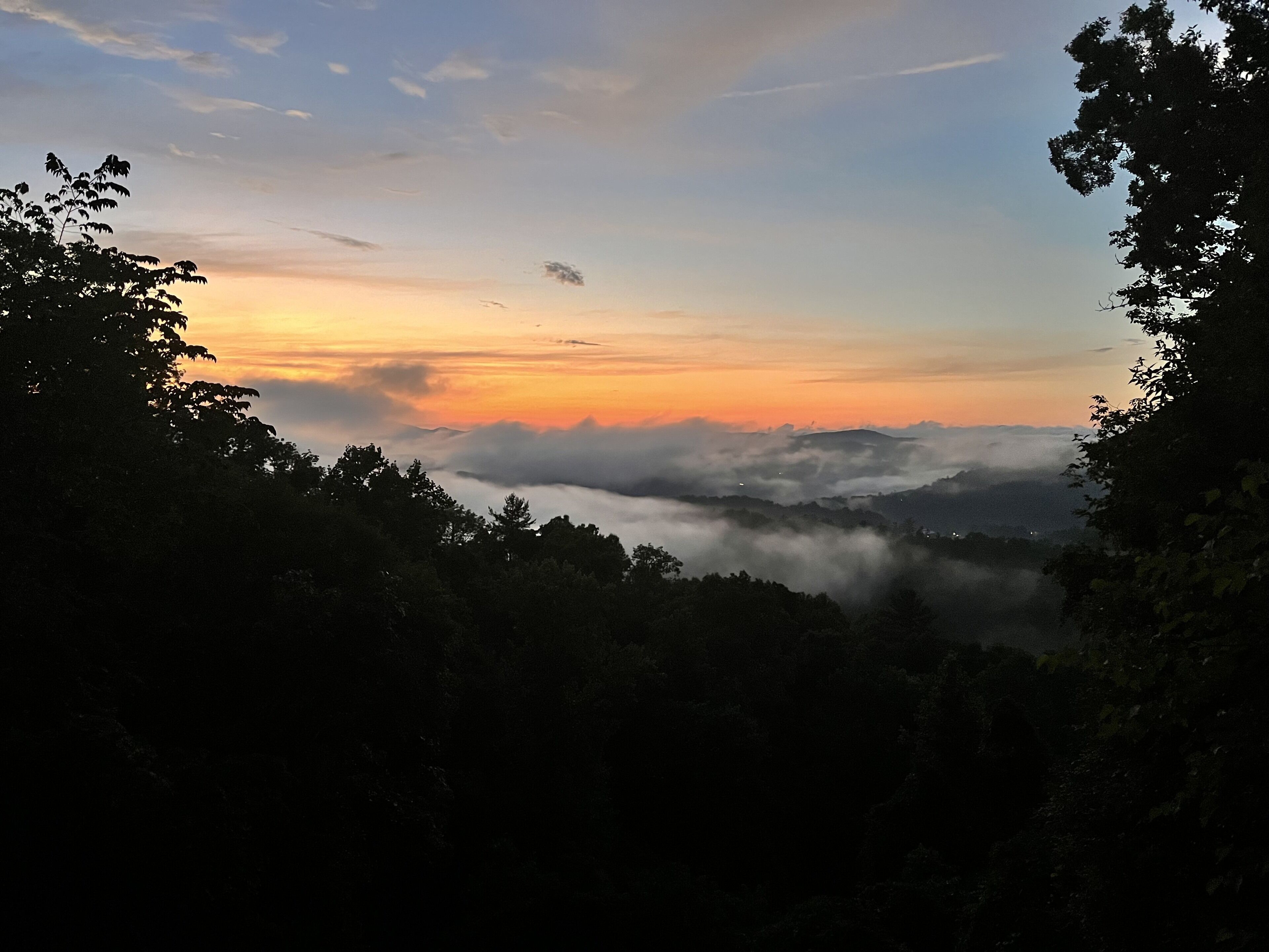 Paisaje montañoso con amanecer o atardecer, que muestra un valle cubierto de niebla y árboles.