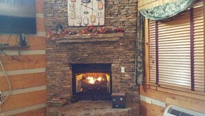 Una chimenea de piedra con un televisor montado encima, una ventana con persianas y un reloj decorativo.
