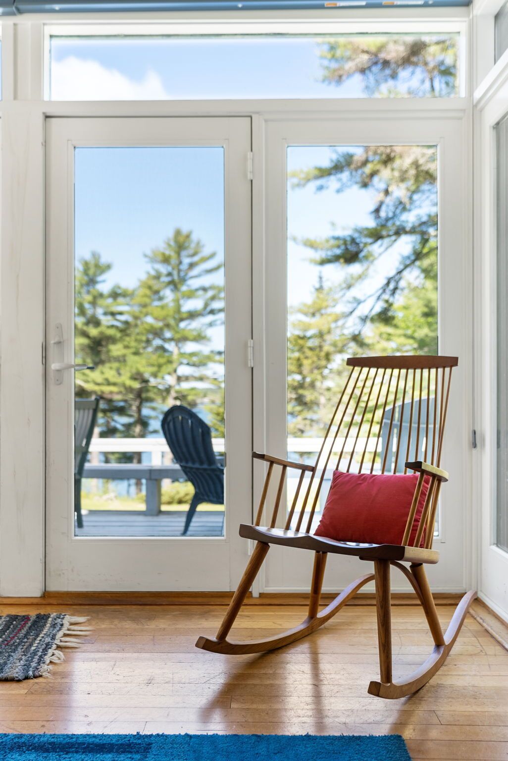 Un fauteuil à bascule avec un coussin rouge, dans une pièce dont le sol est en bois et où se trouve un tapis bleu.