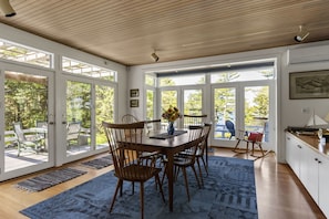 A dining area with a wooden table, six chairs, and a vase with flowers. - Spacious Waterfront Summer Home with Swimming, Kayaking, and Sunsets (Phippsburg)