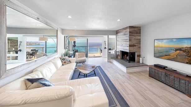 A spacious living room with a large sofa, a coffee table, and a fireplace. There is a television mounted on the wall and a large window providing a view of the ocean. - Spectacular Oceanfront  - the Best Views in Dana Point !!!!! (Dana Point)