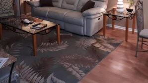 Una sala de estar con un sofá gris, una mesa de centro de vidrio y un tapete estampado. Hay dos lámparas de pared y cuadros enmarcados sobre el sofá.