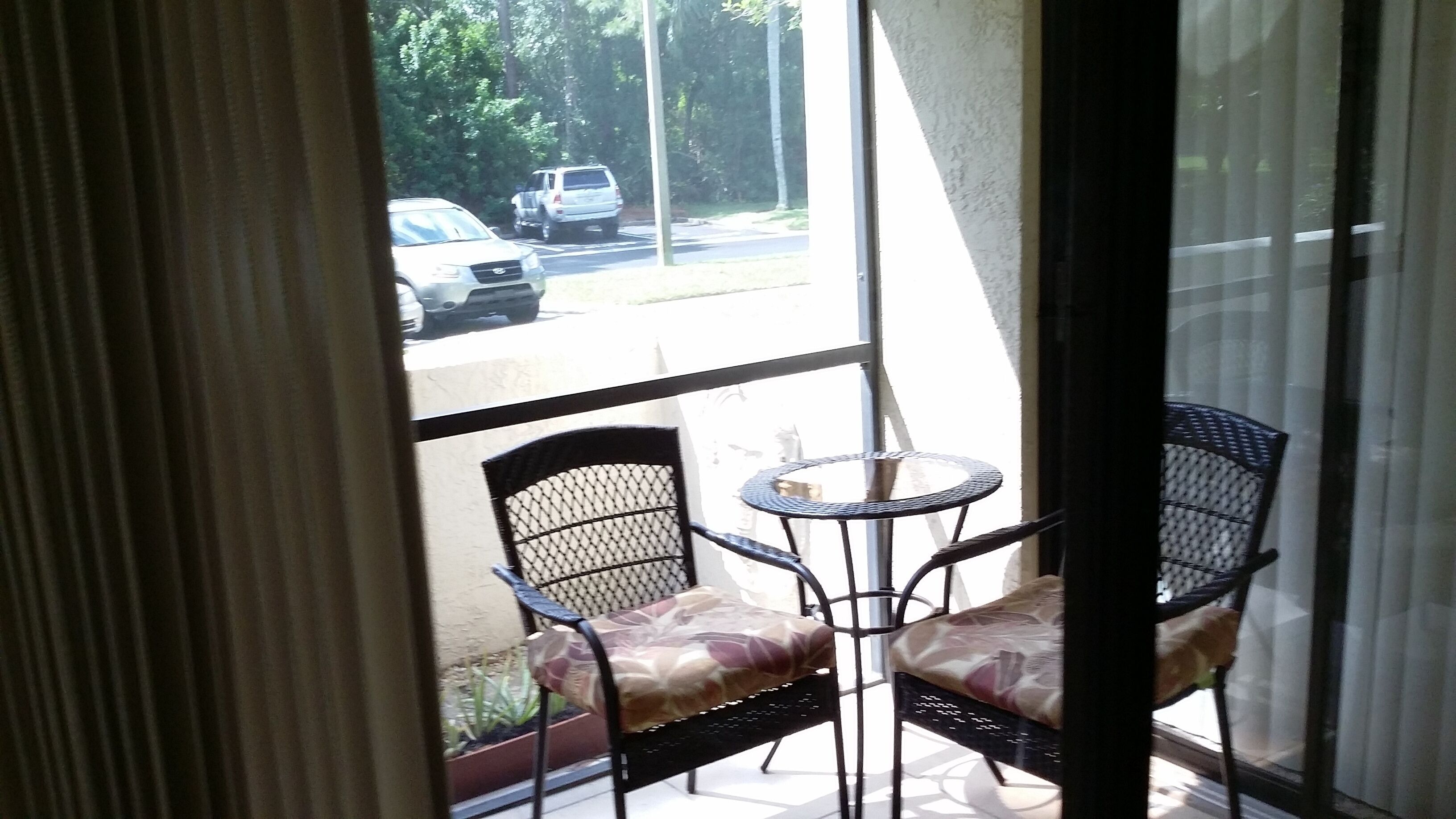 A balcony with two chairs and a small round table, overlooking a street with parked cars.
