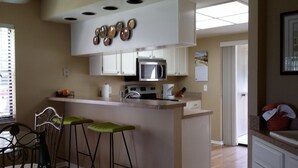 Una cocina con una isla central, taburetes de bar, microondas y estufa.