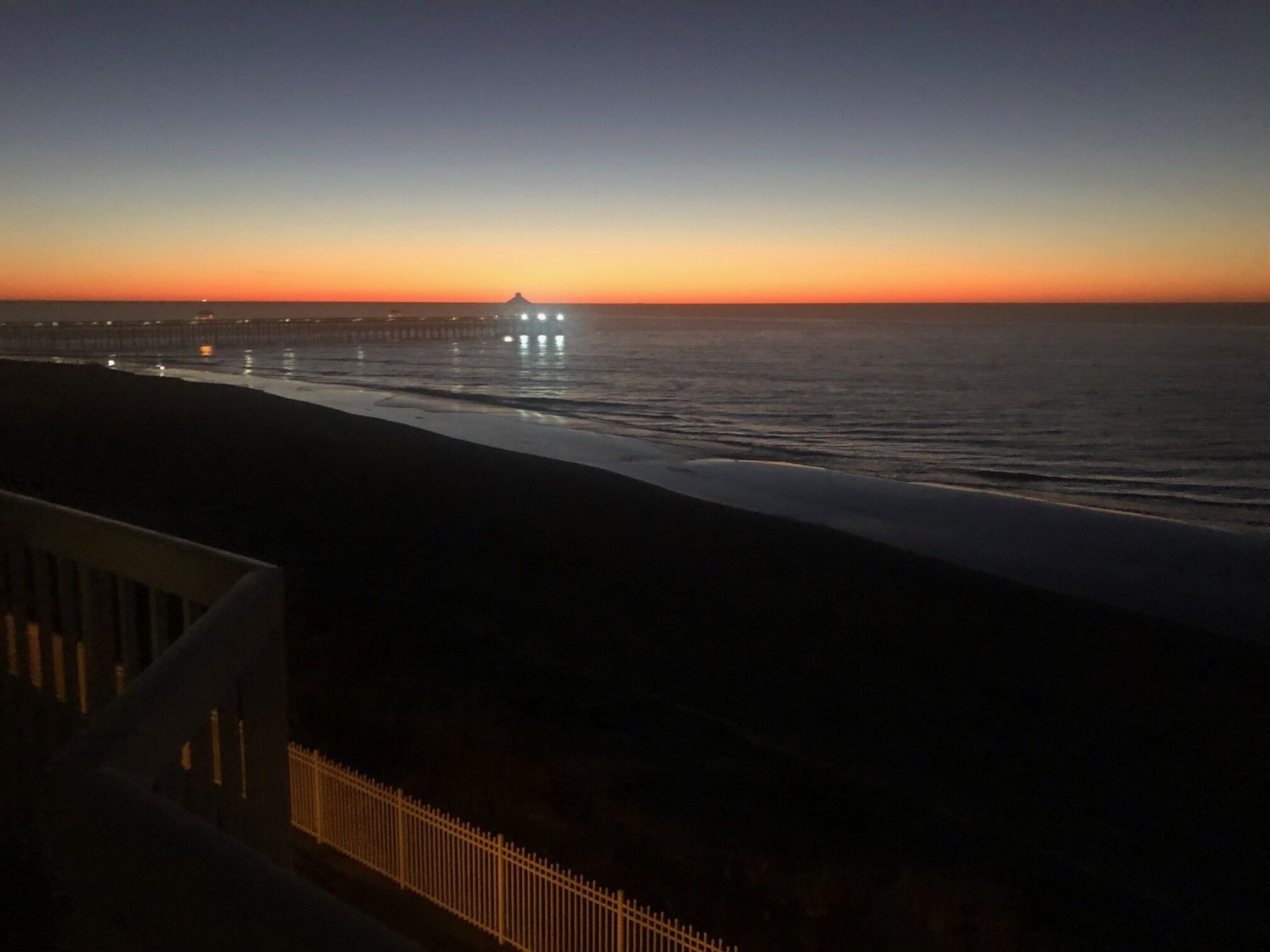 A coastal sunset view with a pier in the distance.