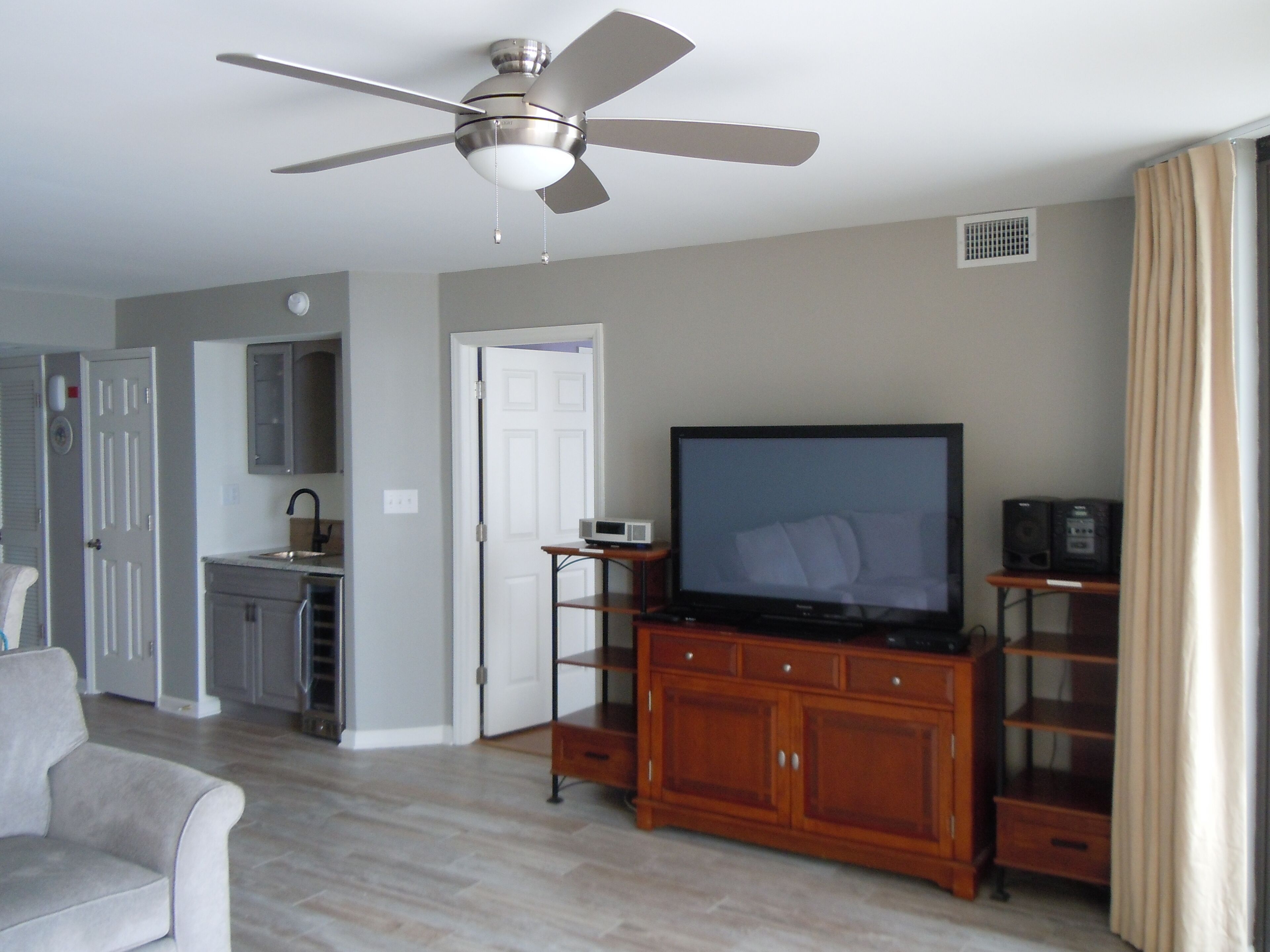 A living room with a flat-screen TV, wooden entertainment center, ceiling fan, and a grey sofa.