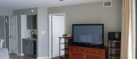 A living room with a flat-screen TV, wooden entertainment center, ceiling fan, and a grey sofa.