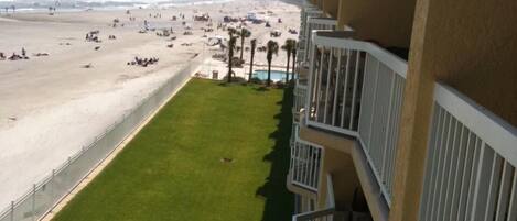 A view from a balcony overlooking a beach with a grassy area and a pool.