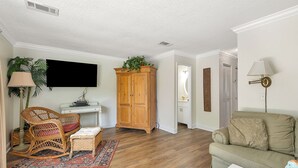 A living room with a wooden floor, a wicker chair, a sofa, a cabinet, and a TV. - YOUR ISLAND DESTINATION IS WAITING! (Saint Simons Island)