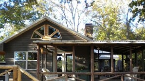 A rustic cabin with a stone foundation, a wooden porch, and a staircase leading to the entrance. - Lake Cabin on the Bluff (Hot Springs)