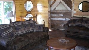 A log cabin interior with a wooden ceiling, a round table, two sofas, and a mirror on the wall. - Lake Cabin on the Bluff (Hot Springs)