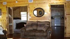 A cozy cabin interior with a wooden interior, a sofa, a dining table, and a kitchen area. - Lake Cabin on the Bluff (Hot Springs)