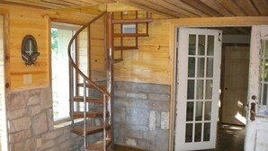 A wooden interior with a spiral staircase, stone walls, and a white door. - Lake Cabin on the Bluff (Hot Springs)