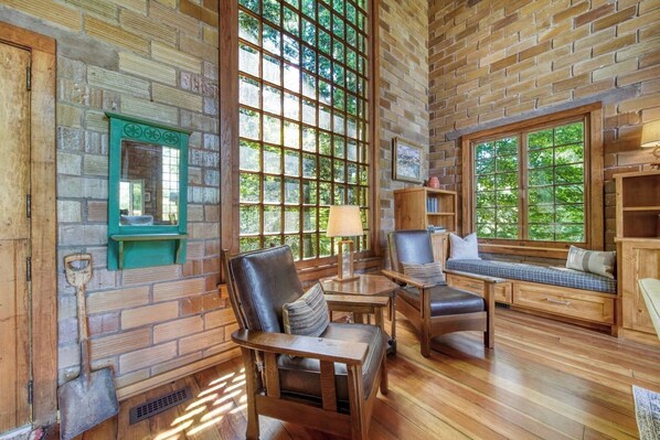 A rustic interior with wooden walls, large windows, and a seating area with a bench and chairs.