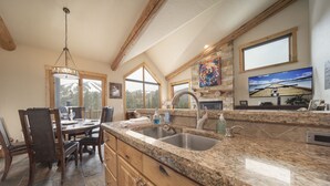 A kitchen with granite countertops, wooden cabinets, a large window, and a dining area with a chandelier.