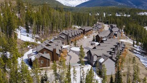 A resort with multiple chalet-style buildings arranged in a row, surrounded by dense forests and snow-covered mountains.